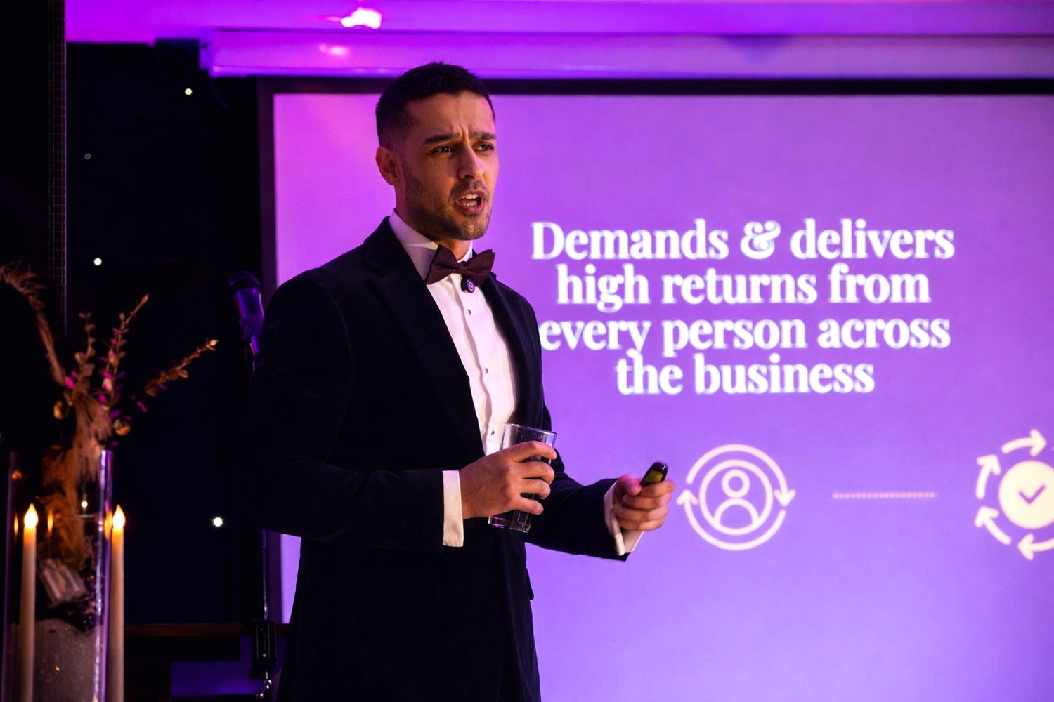 Roheel Ahmad on stage in front of a slide reading: Demands and delivers high returns from every person across the business